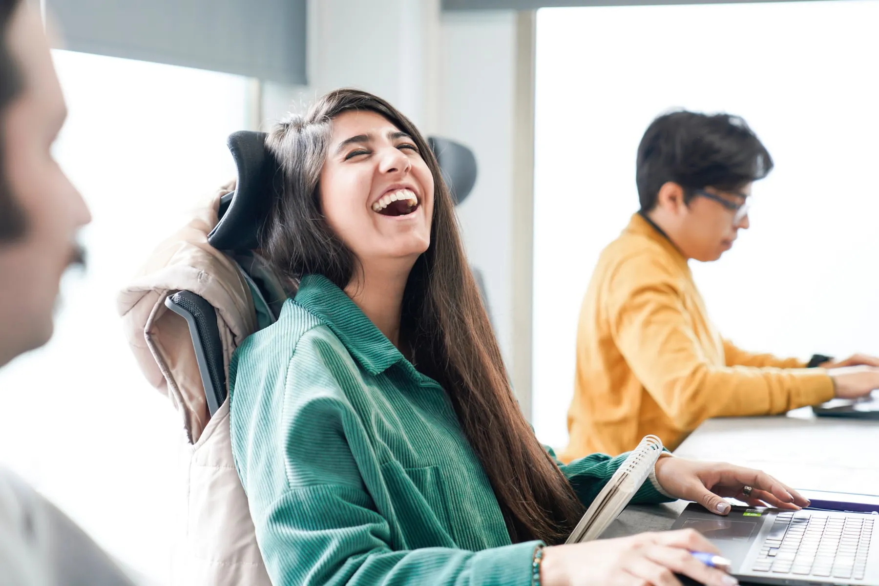 A woman laughing at her desk while a colleague works beside her