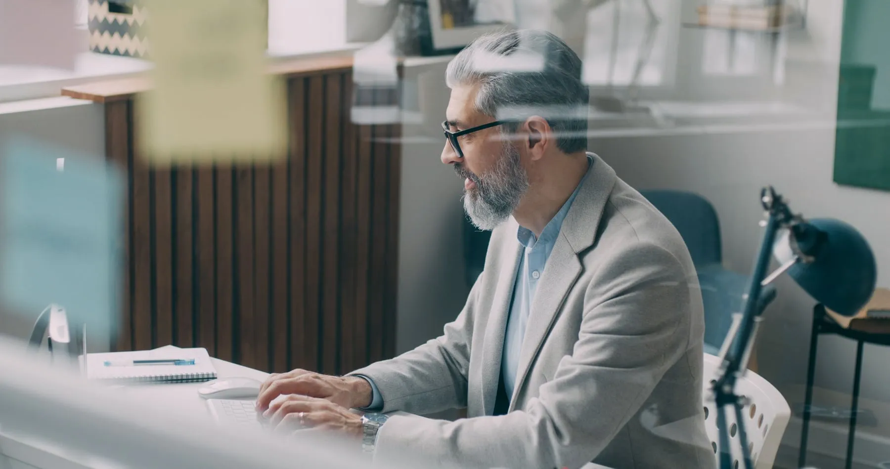A man with a grey beard and glasses working at a laptop in an office
