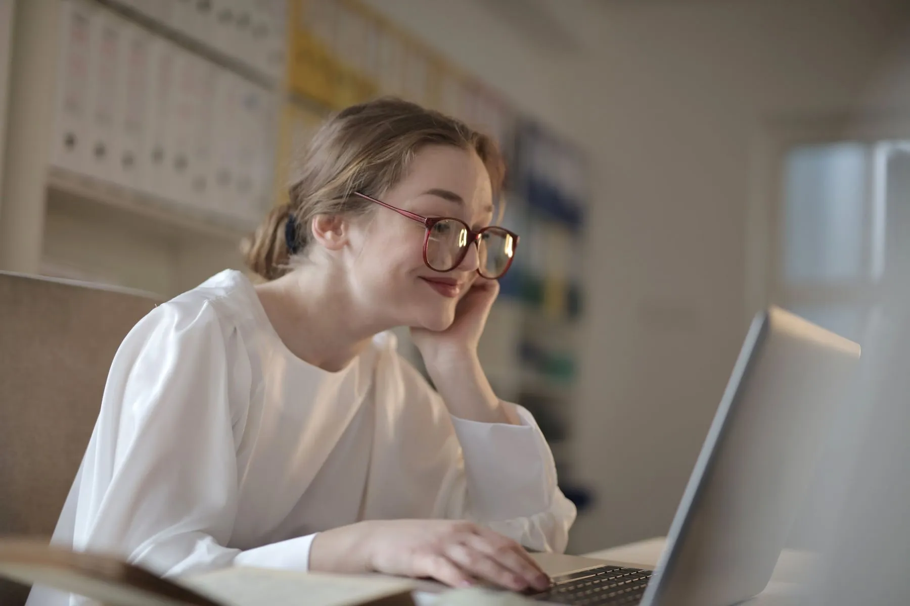 A woman in a white blouse smiling at a laptop in an office