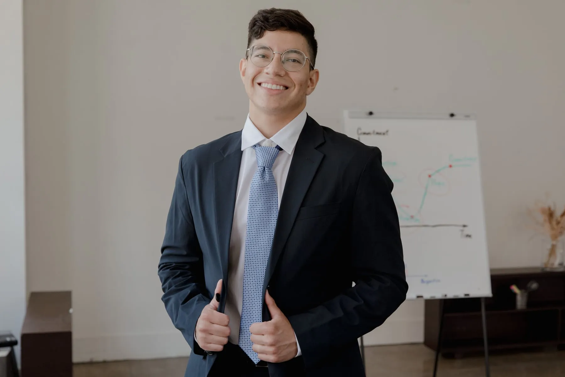 A smiling man in a suit and tie standing in front of a whiteboard
