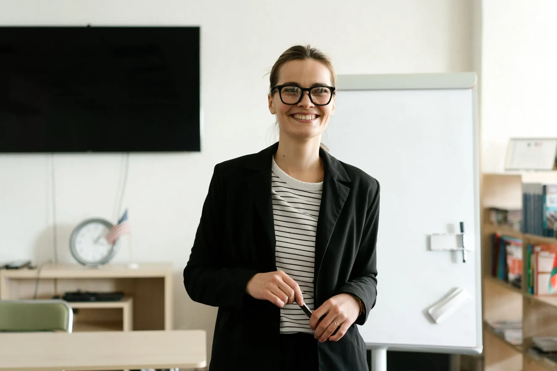 A woman in glasses and a dark blazer smiling in a bright office